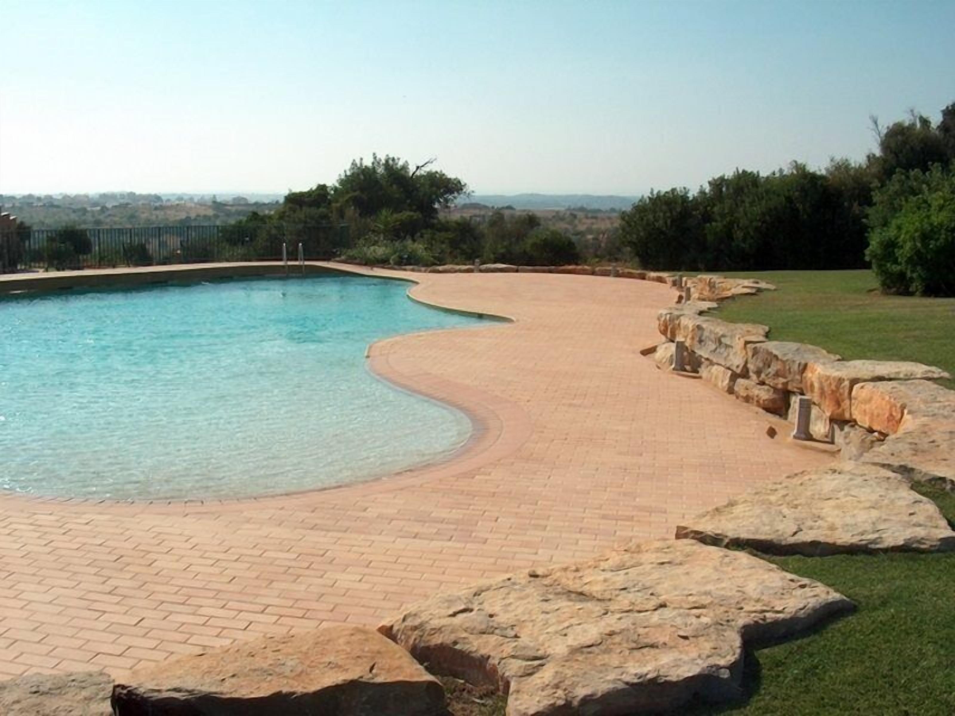 A swimming pool with a curved edge, surrounded by a brick patio and stone steps leading into the water.