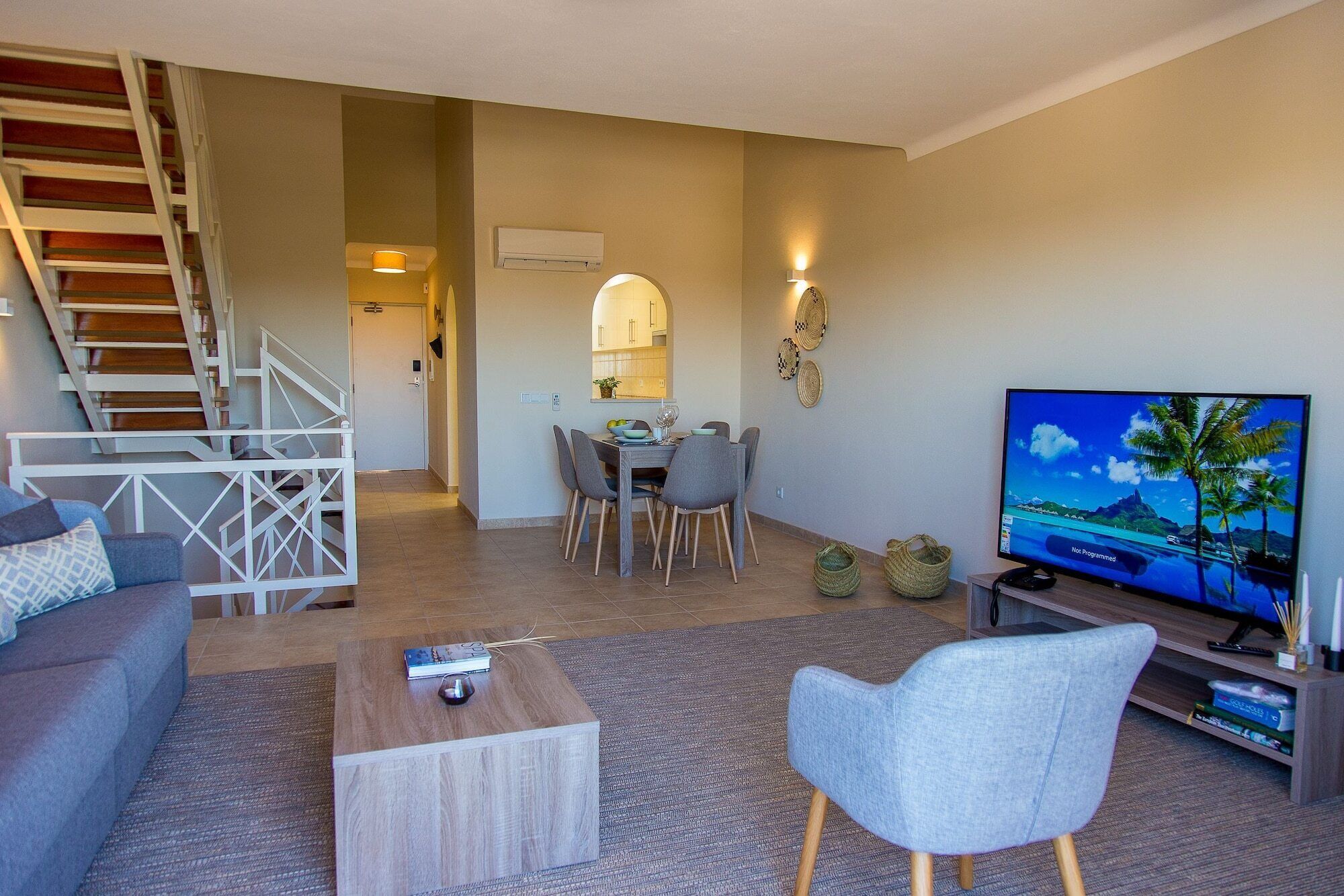 A living room with a sofa, coffee table, TV, and a staircase leading to a dining area.