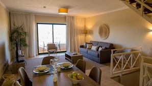A modern living room with a sofa, dining table, and chairs. There is a staircase in the background. - Noria Velha (Lagoa)