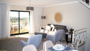 A modern living room with a sofa, chairs, a dining table with wine glasses, a view of the outdoors, and a staircase. - Noria Velha (Lagoa)