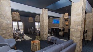 A modern lounge area with stone pillars, grey sofas, and a flat-screen TV mounted on a wall. - Noria Velha (Lagoa)