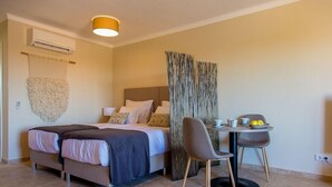 A hotel room with a bed, a small table with chairs, an air conditioning unit, and a wall-mounted light fixture. - Noria Velha (Lagoa)