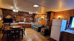 A cozy cabin interior with a wooden dining table, chairs, a sofa, and a kitchen area with a refrigerator and stove. - Blakley Hobbit Large Cabin (Viola)