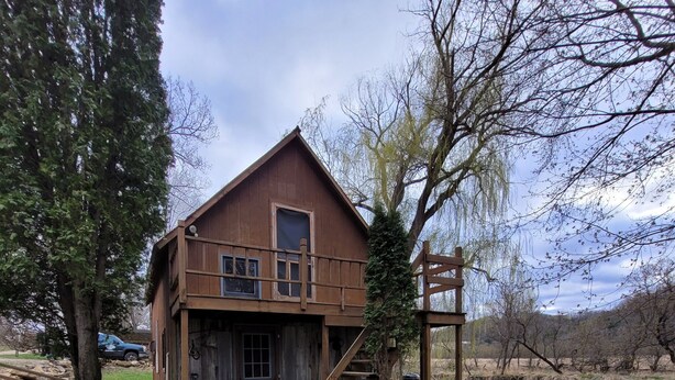 A rustic wooden cabin with a front porch, a staircase, and a small deck area. - Blakley Hobbit Large Cabin (Viola)