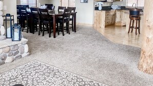 Een ruime woonkamer met een eettafel, stoelen, een keuken met houten kastjes en een trap naar een hoger niveau.