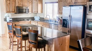 Een moderne keuken met houten kastjes, een roestvrijstalen koelkast en een centraal kookeiland met barstoelen.