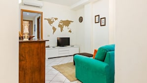 Una sala de estar con un sofá color turquesa, un aparador de madera, un televisor sobre un soporte blanco, un mapa mundial en la pared y un reloj.