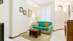 Un salón con un sofá azul verdoso, un reposapiés marrón, un televisor y cuadros en la pared.