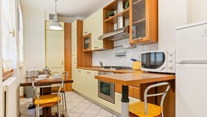Una cocina compacta con armarios de madera, estufa a gas, microondas y comedor con sillas metálicas.