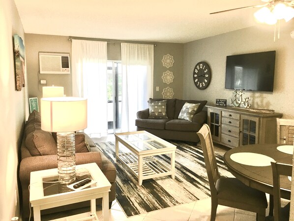 A living room with a sofa, coffee table, TV, and a dining area with a table and chairs.