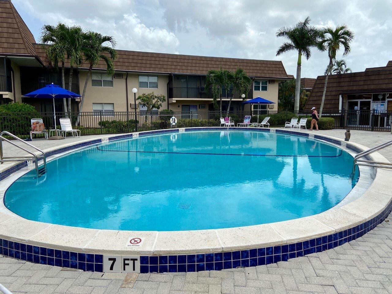 A swimming pool with a 7 ft depth, surrounded by lounge chairs and umbrellas, with a building in the background.