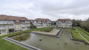 Un complejo residencial con varios edificios de apartamentos, un patio central con un estanque y abundante vegetación.