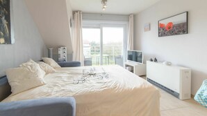 Un dormitorio moderno con una cama grande, televisor, radiador y balcón con vistas.
