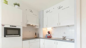 Una cocina moderna con armarios blancos, horno empotrado, microondas, cafetera y un lavabo.