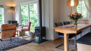 Un salon moderne avec un poêle à bois, une table à manger avec des chaises, un canapé et une grande fenêtre avec des rideaux.
