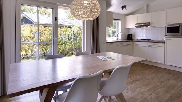 Une cuisine moderne avec des meubles blancs, une table à manger en bois et un luminaire suspendu.