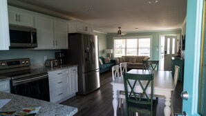 A kitchen with white cabinets, stainless steel appliances, and a dining area with a white table and green chairs.