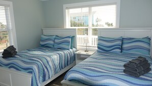 A bedroom with two beds, each with a blue and white striped bedspread, white headboards, and a nightstand with a lamp between the beds.
