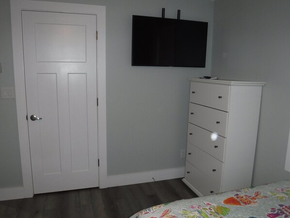 Una camera da letto con una porta bianca, un comò bianco e una TV a schermo piatto montata a parete.