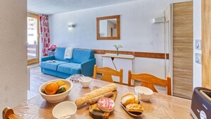 Ein gemütliches Wohnzimmer mit einem blauen Sofa, einem Esstisch mit Brot und Obst sowie einer Küchenzeile mit einem Toaster.