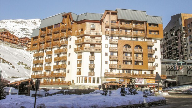 Ein mehrstöckiges Hotel mit hölzernen Balkonen und Skipisten im Hintergrund.