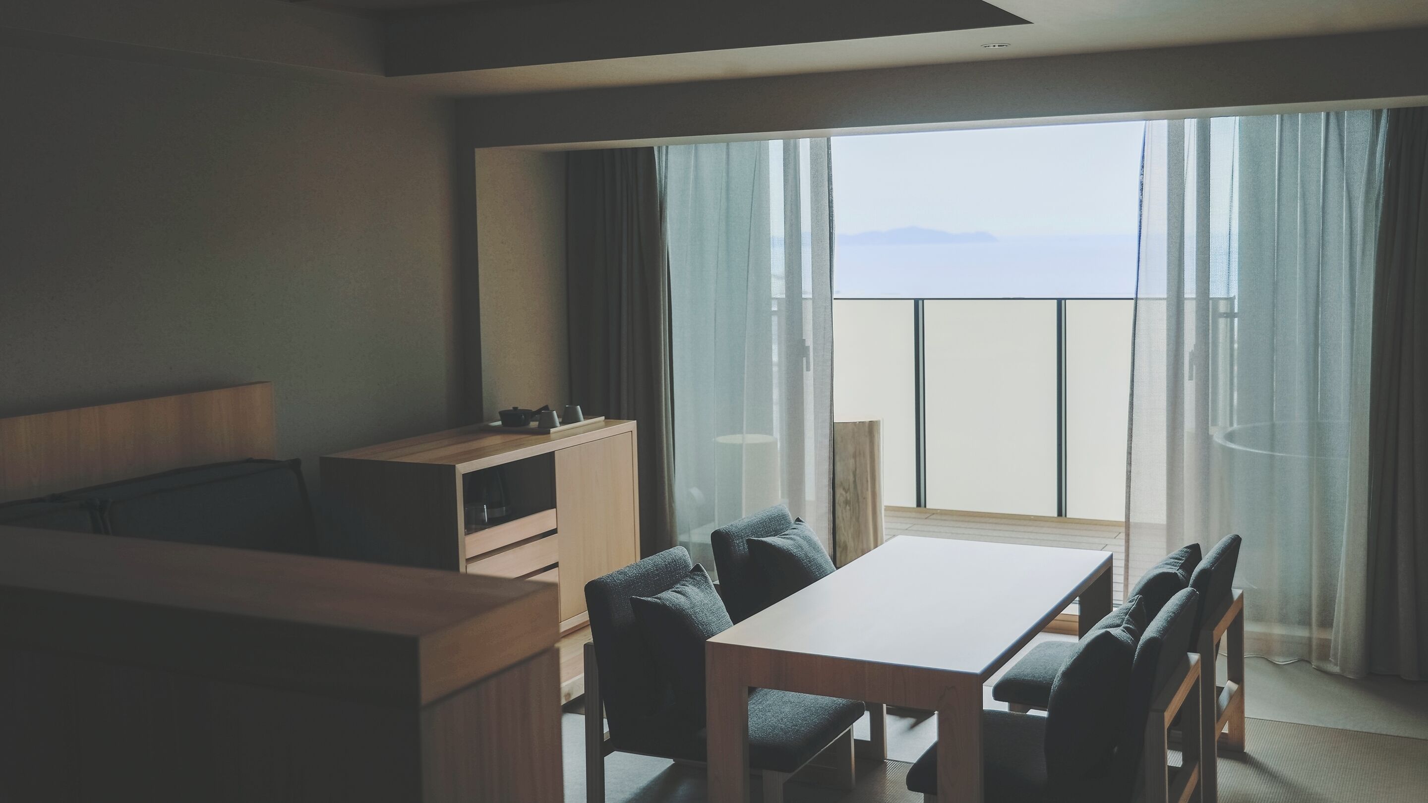 A hotel room with a balcony, a wooden desk, a chair, a sofa, and a TV.