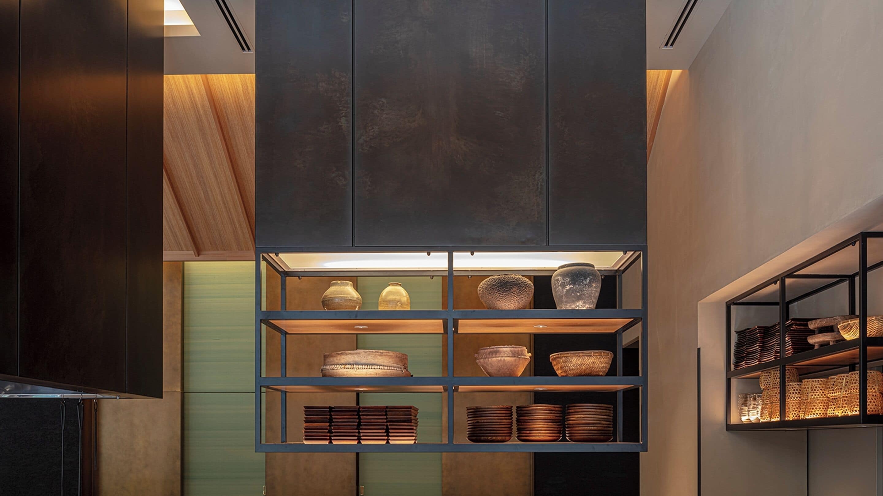 Une cuisine moderne avec des meubles de rangement sombres, des étagères en bois et divers ustensiles de cuisine.