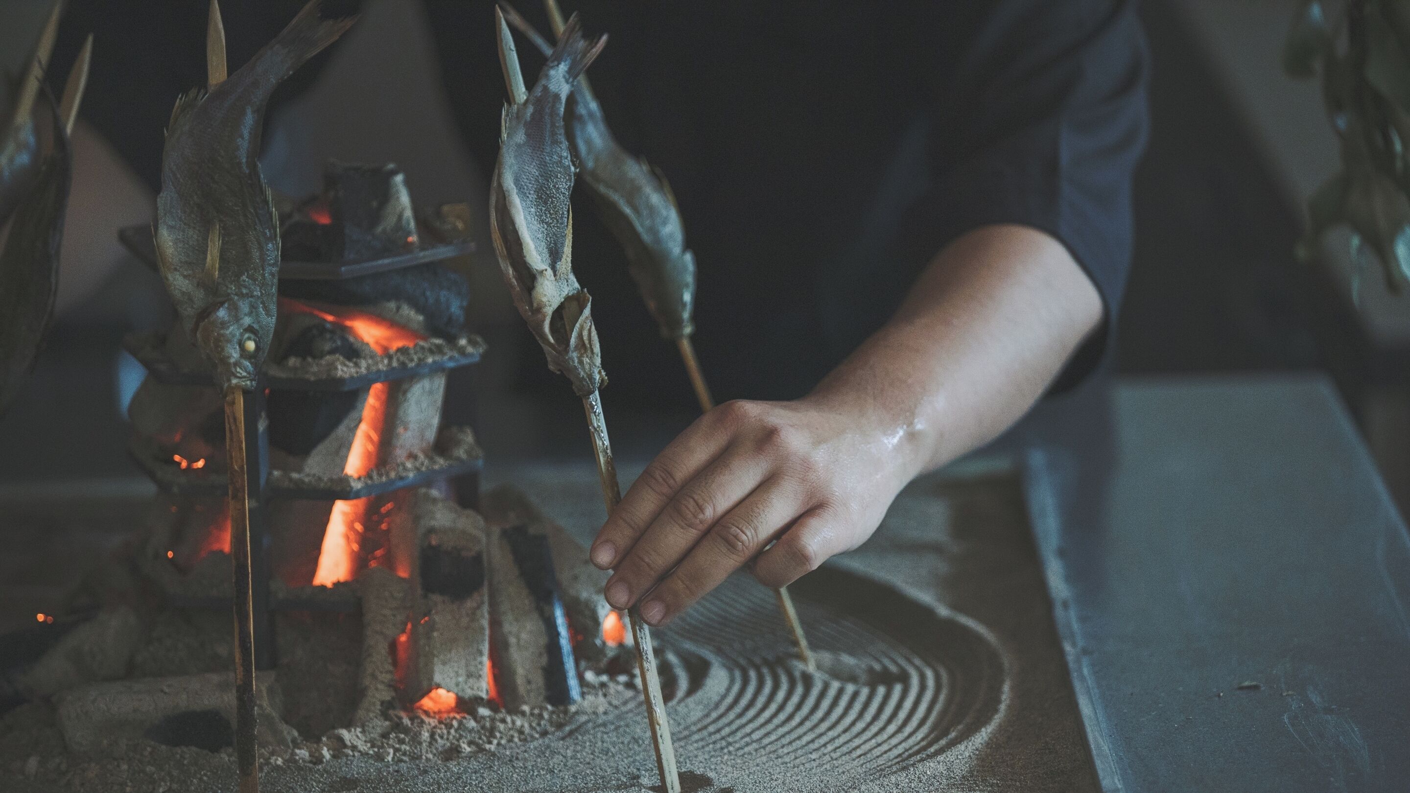 Eine Hand hält einen Metallstab über einem Feuer.