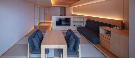 Een moderne woonkamer met een houten eettafel, blauwe banken en een televisie.
