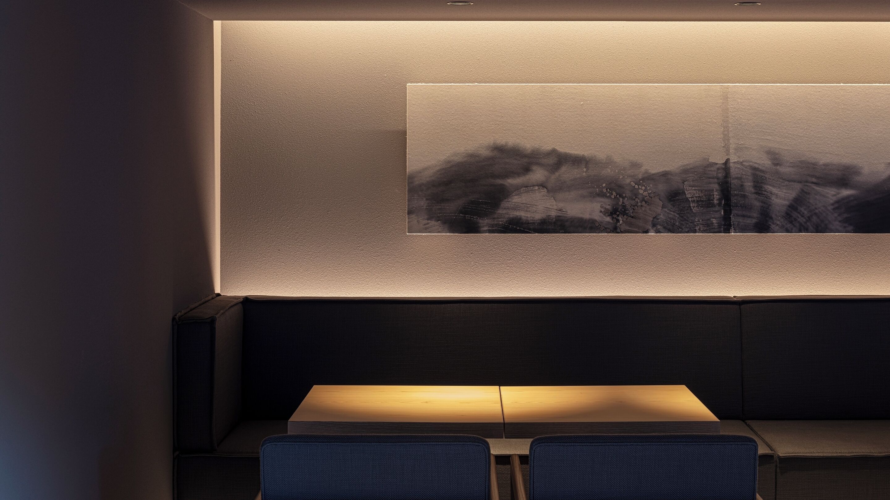Un intérieur moderne avec un canapé de couleur sombre et deux fauteuils bleus placés face à une œuvre d’art accrochée au mur.