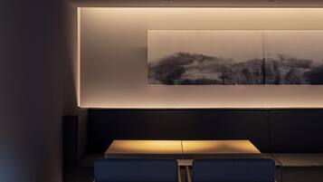 Un interior moderno con un sofá de color oscuro y dos sillas azules frente a una obra de arte colgada en la pared.