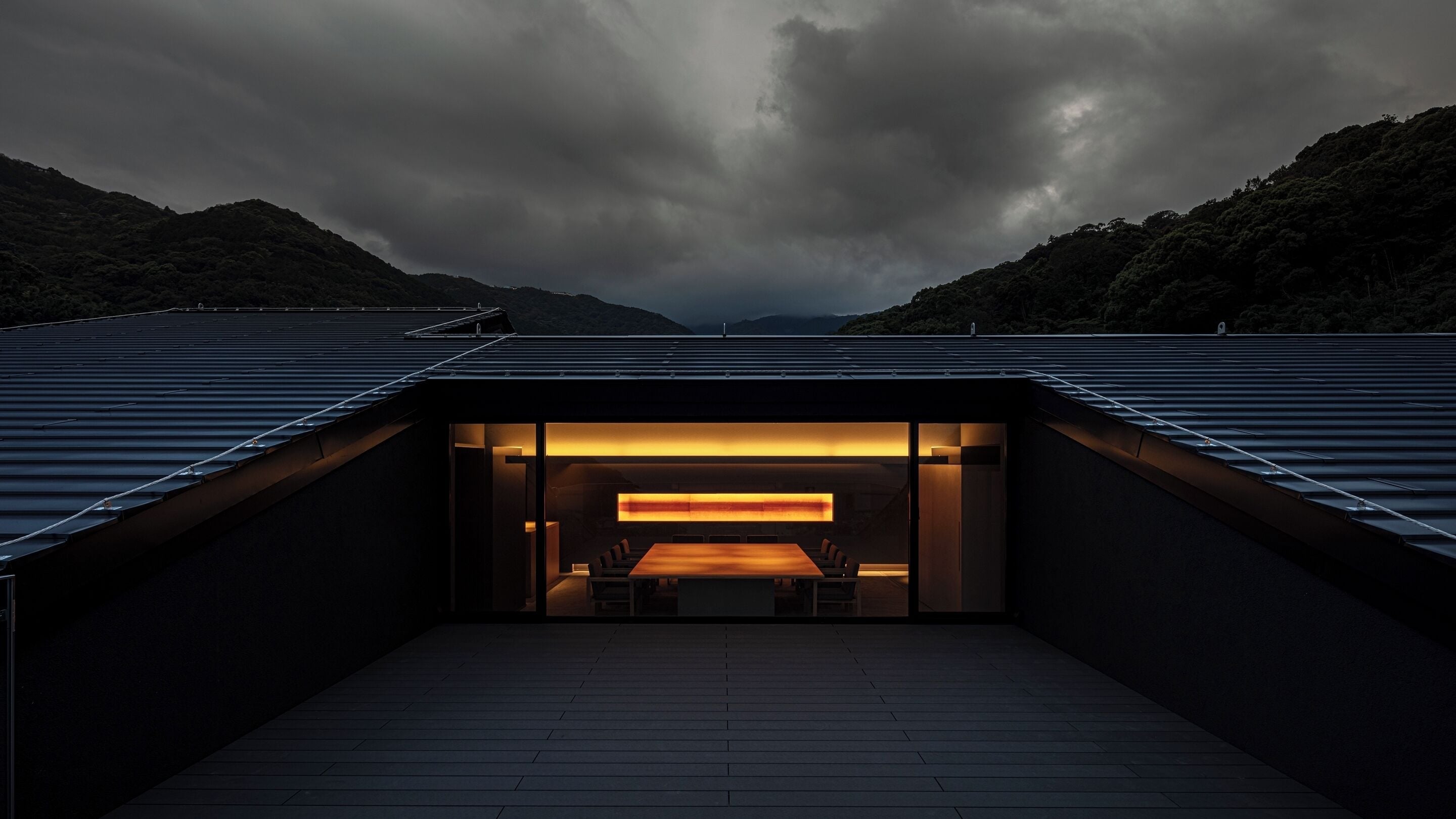 A modern building with a central open space, surrounded by metal roofing, and a view of a mountainous landscape.