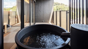 Un jacuzzi con agua fluyendo, una terraza de madera y vistas a una zona boscosa.