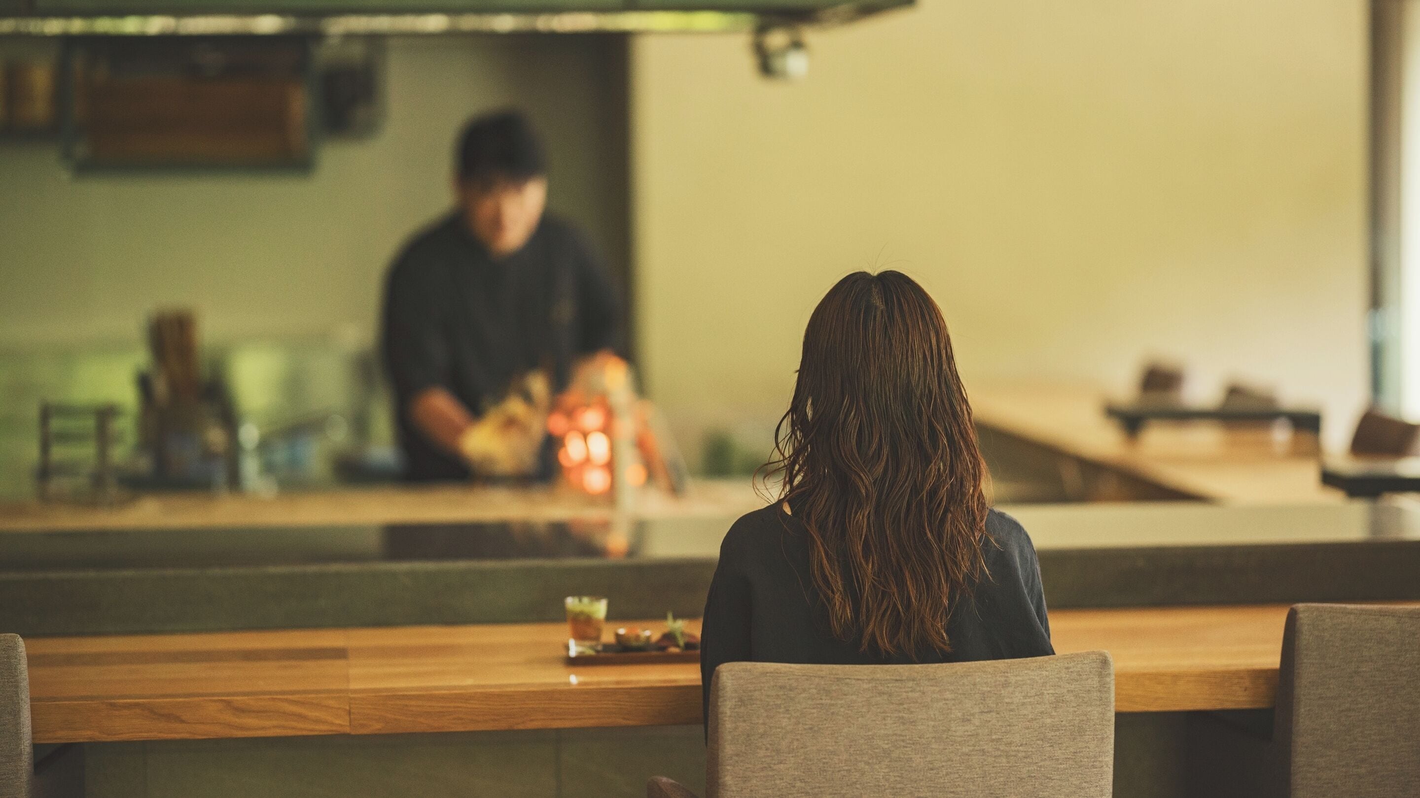 Eine Person sitzt an der Theke in einem Restaurant, im Hintergrund ist ein Barbereich zu sehen.