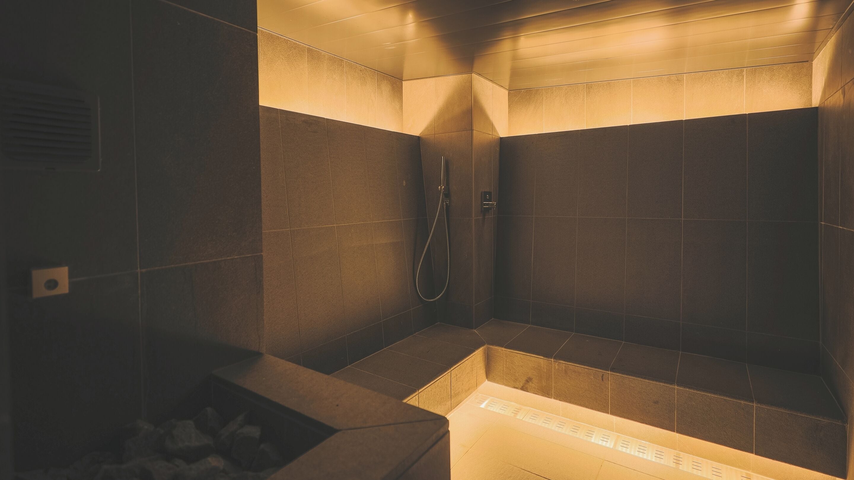 A modern shower area with dark tiles and a built-in bench.