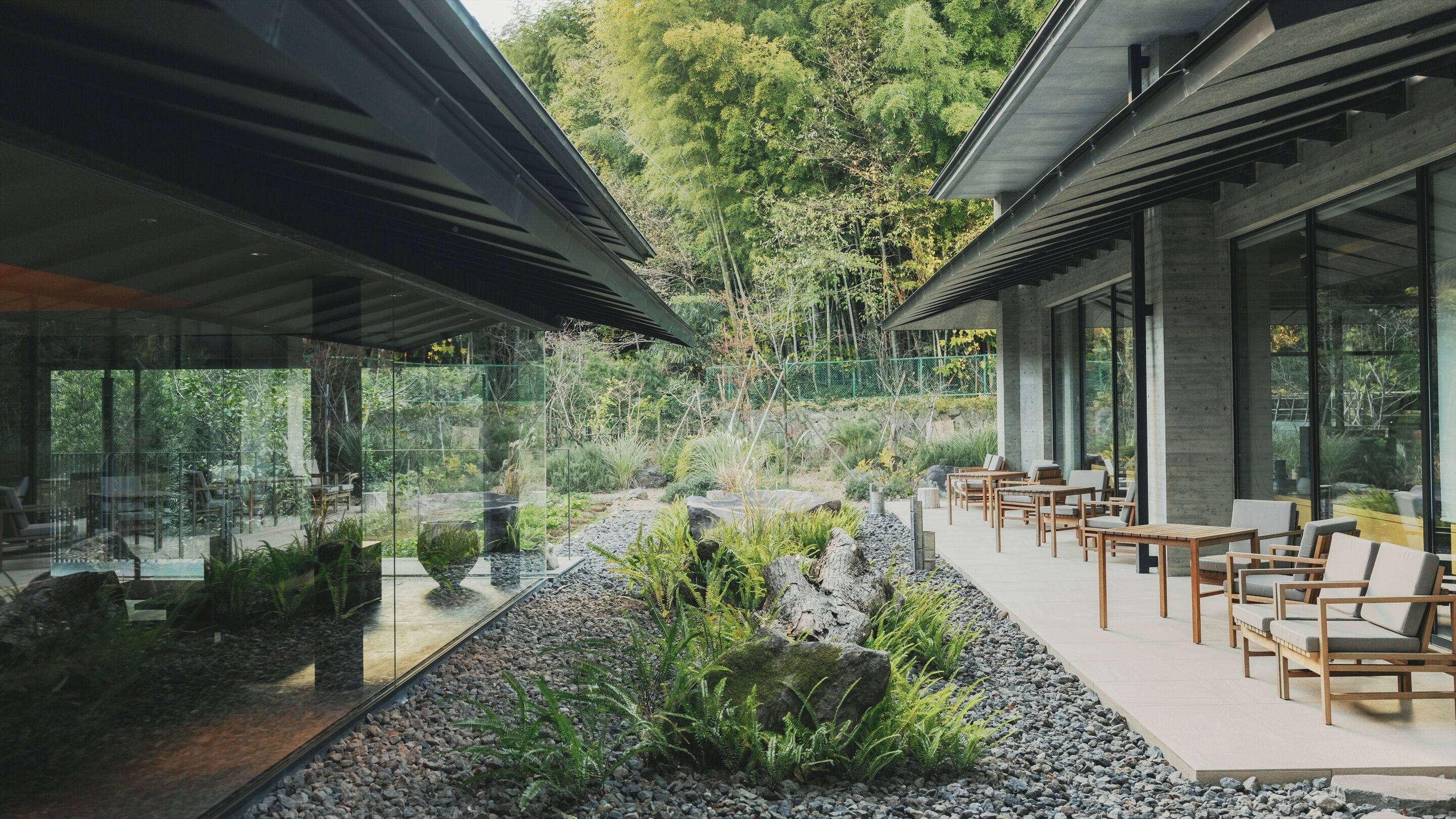 A modern outdoor seating area with tables and chairs, surrounded by a garden with rocks and plants.
