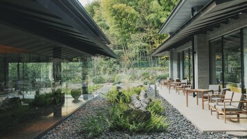 Una zona relax esterna moderna con tavoli e sedie, circondata da un giardino con rocce e piante.
