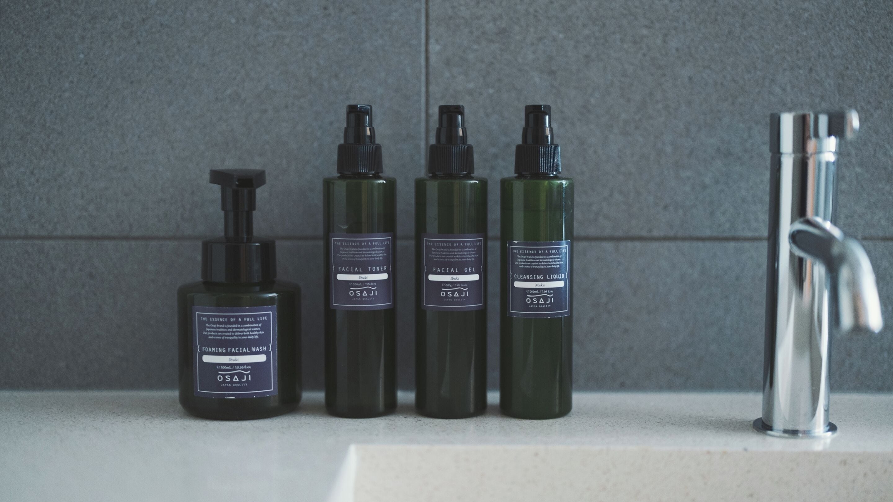 Cuatro botellas de productos para el cuidado facial sobre una encimera de baño junto a un lavabo.