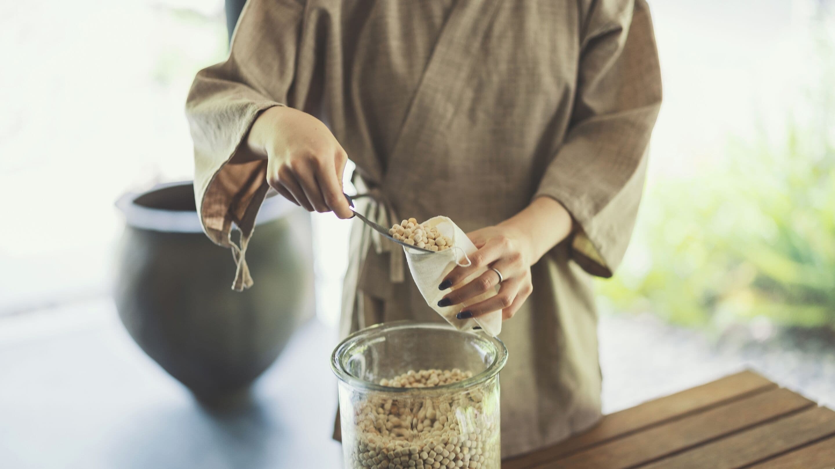 A person scooping chickpeas from a cloth into a glass jar.