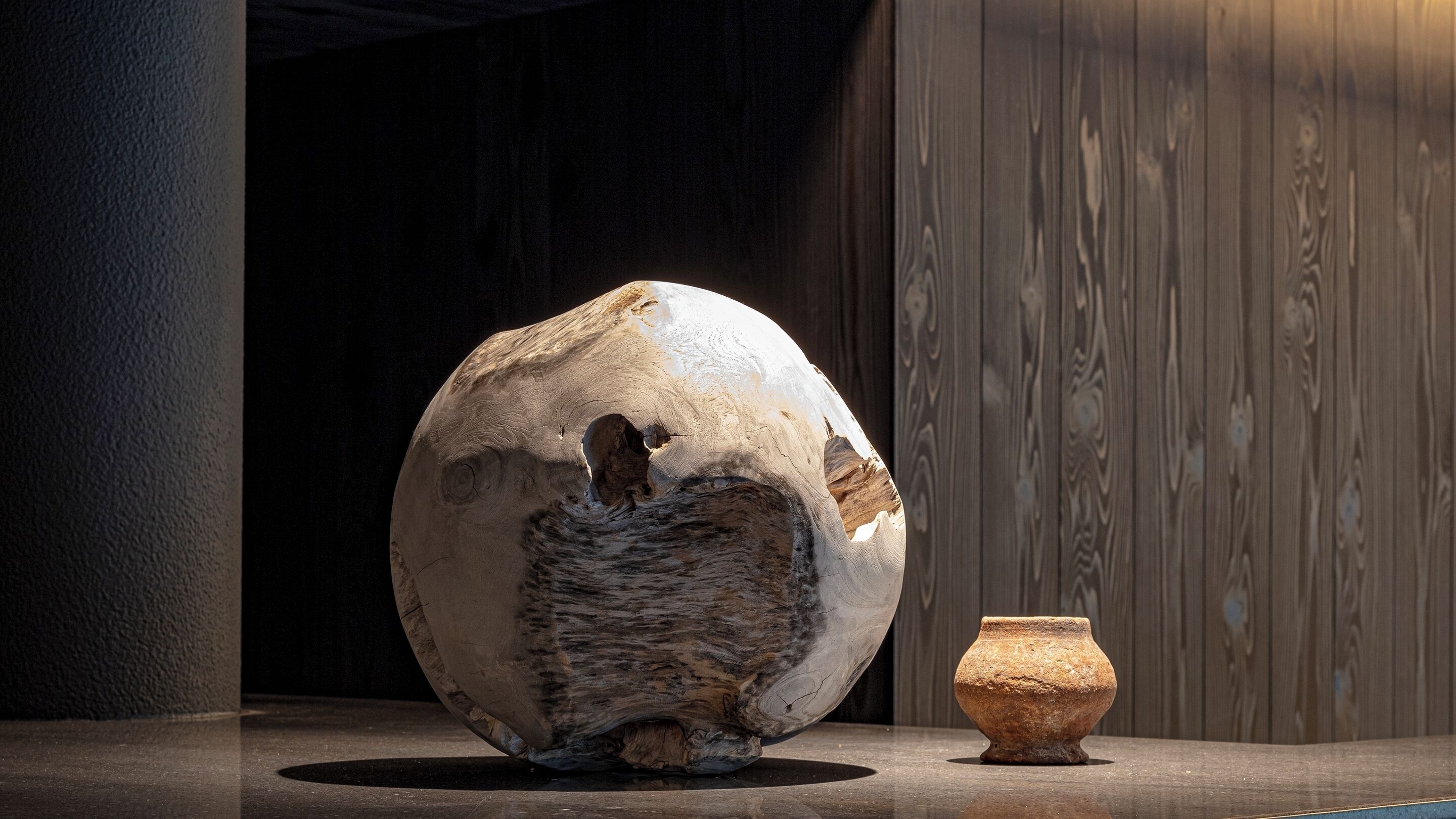A large, irregularly shaped stone sculpture and a small, round pottery piece on a reflective surface.