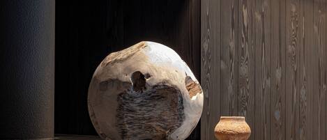 A large, irregularly shaped stone sculpture and a small, round pottery piece on a reflective surface.
