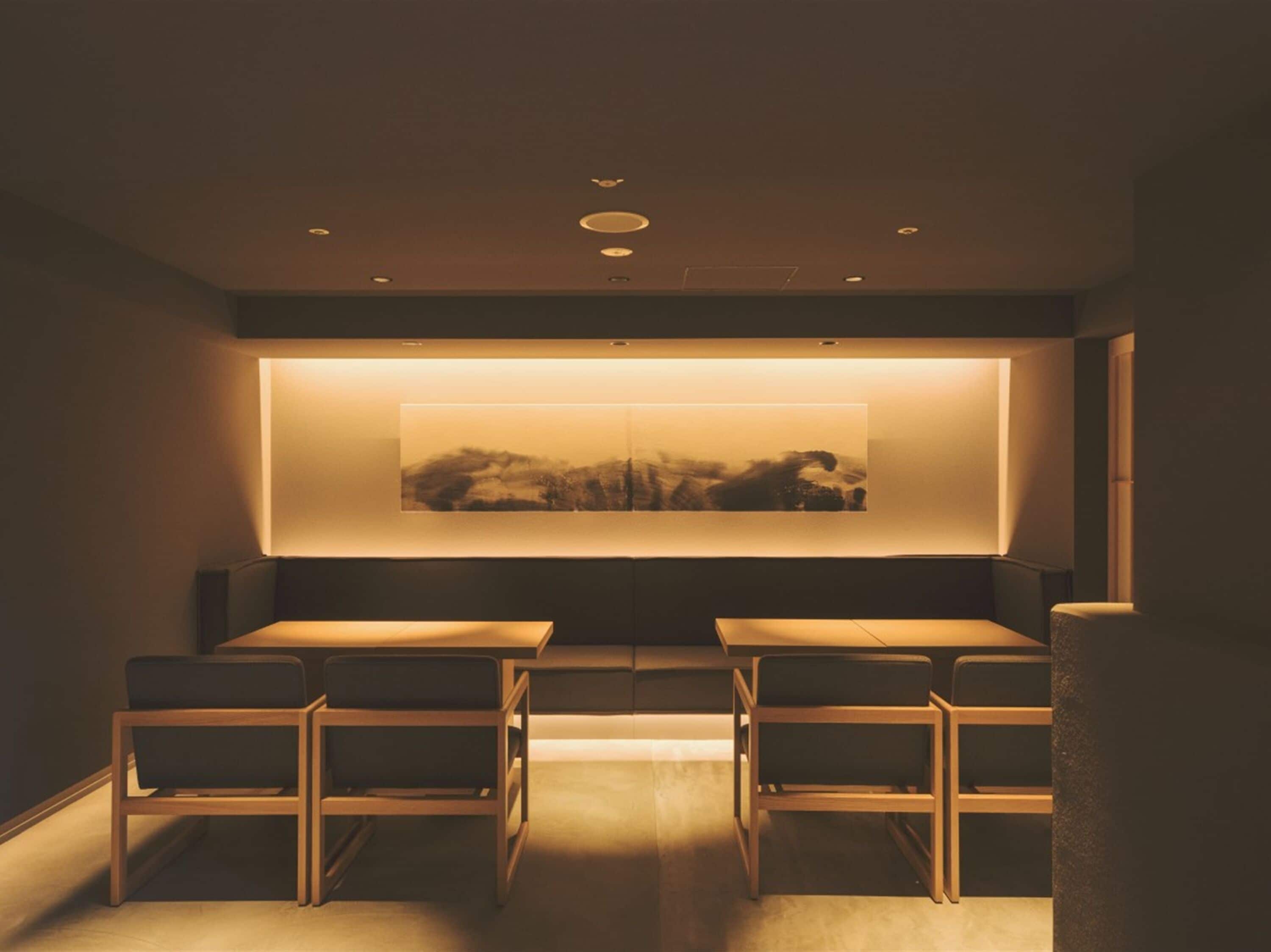 A modern room with two tables and chairs, a large abstract painting on the wall, and recessed ceiling lighting.