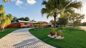 A residential area with a paved driveway leading to a house, surrounded by well-maintained grass and palm trees. - Hidden Gem Villa | Heated Pool, Hot Tub & Tikihut (Fort Lauderdale)