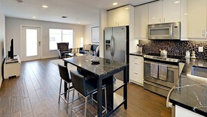 A modern kitchen with stainless steel appliances, a marble countertop, and a dining area with a black table and chairs. - Hidden Gem Villa | Heated Pool, Hot Tub & Tikihut (Fort Lauderdale)