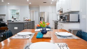 Una cocina moderna con armarios blancos, una isla central con un fregadero y un comedor con una mesa de madera para cuatro.