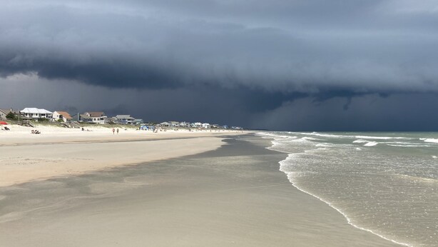 A beach with houses in the background and a stormy sky.