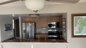 A compact kitchen with a refrigerator, microwave, oven, and a ceiling fan.