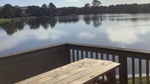 A wooden deck with a table and benches overlooking a calm lake with a distant shoreline.