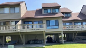 A two-story building with a covered patio area, a car parked under the structure, and a lawn in the foreground.