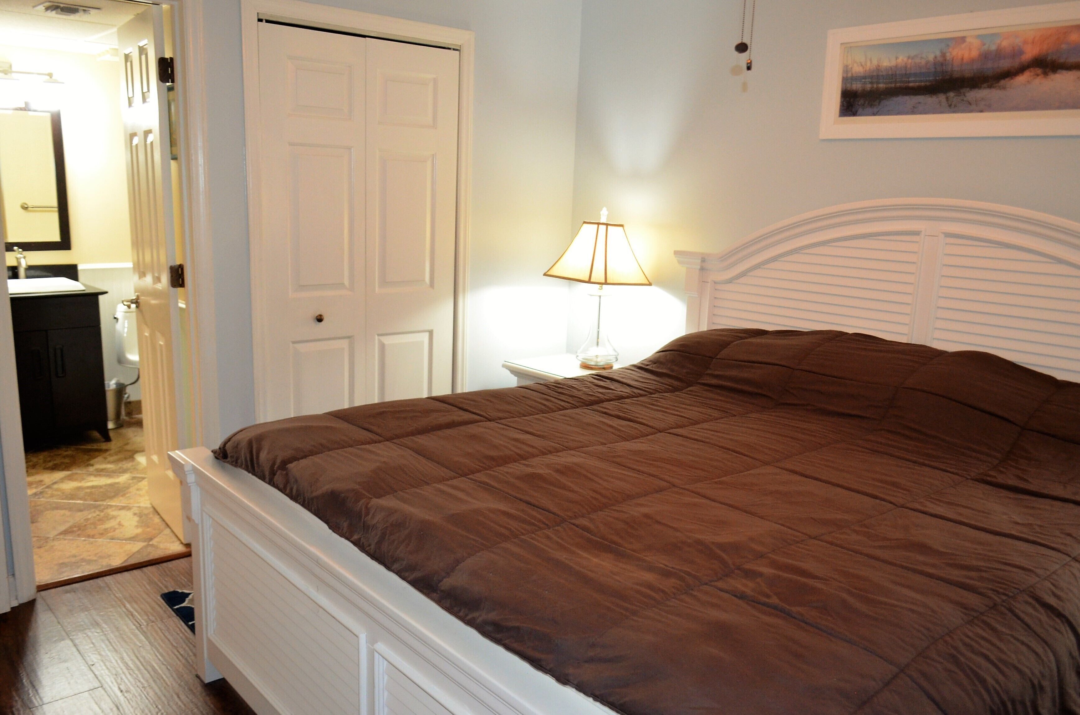 Une chambre à coucher avec un lit, une table de chevet, une lampe, une porte et un tableau au mur.